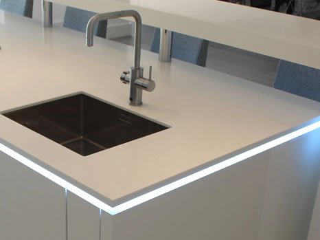 White kitchen island with a white acrylic worktop embedded with LED strip lights around the edge
